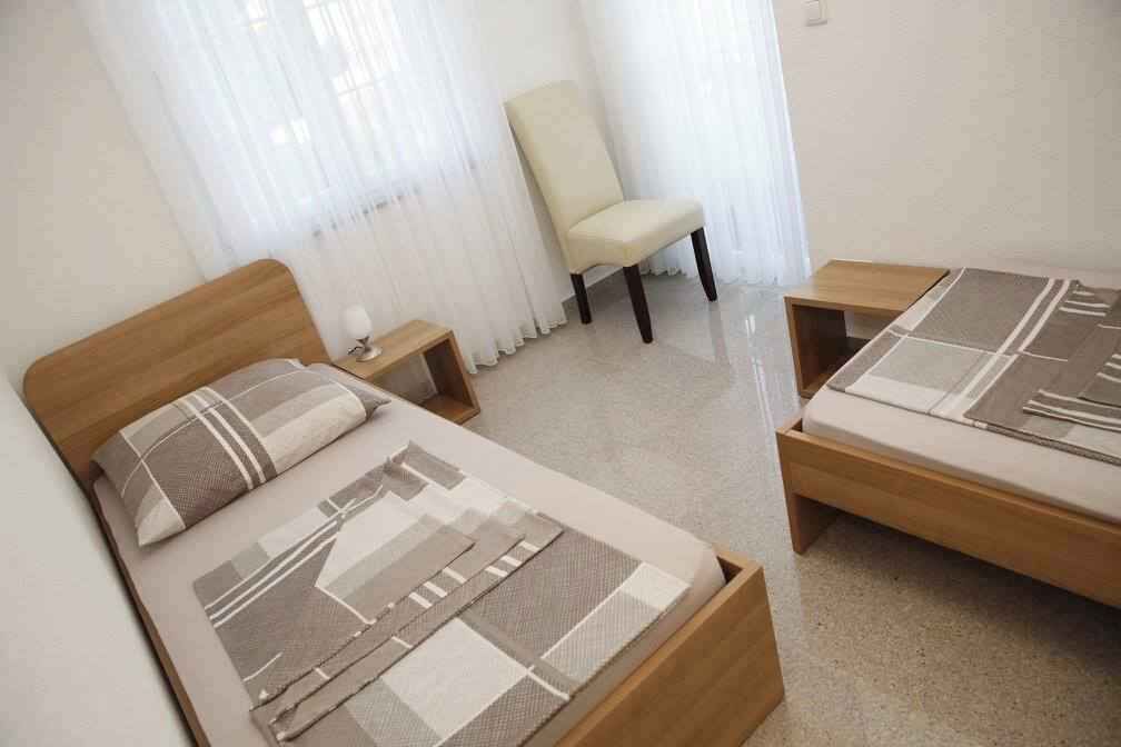 A bedroom with two beds, a chair, a bedside table, and a window with curtains.
