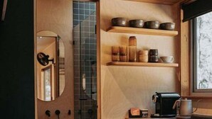 A compact kitchen with a washing machine, a coffee maker, and shelves with dishes.