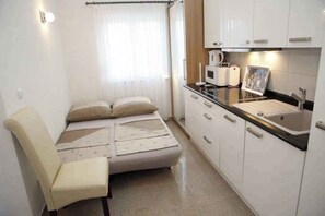 A compact room with a bed, a chair, a kitchenette, and a window with curtains. - Studio ŽELJKA Š. APT 4 (2+0) (Vodice)