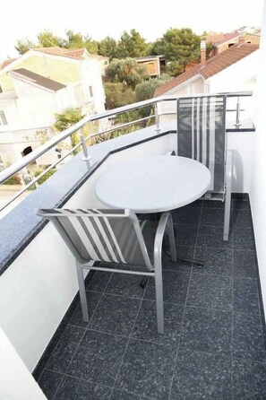 Ein Balkon mit rundem Tisch, zwei Stühlen, einem Metallgeländer und Blick auf umliegende Gebäude und Bäume.