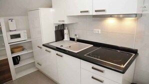 Et moderne køkken med hvide skabe, en sort bordplade, en indbygget komfur, en vask og en mikroovn.