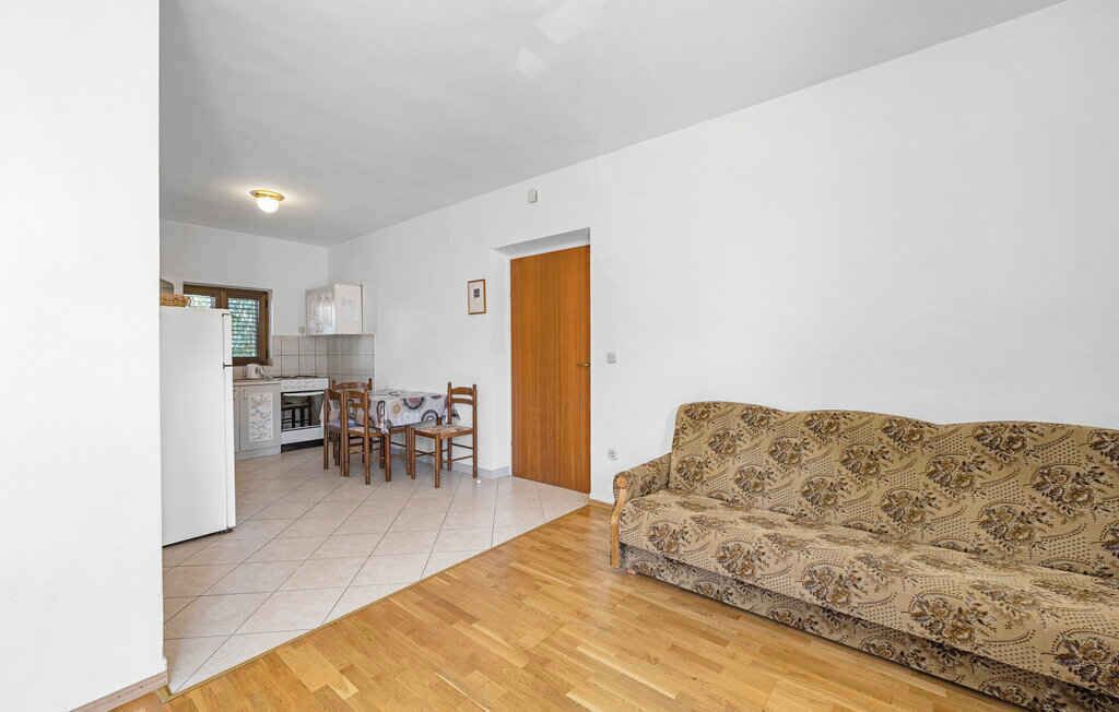 Una sala de estar con un sofá estampado, una zona de comedor con sillas y una mesa, y una cocina al fondo.