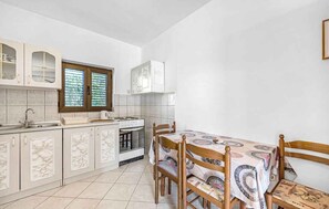 A kitchen with white cabinets, a stove, and a dining table with chairs. - Holiday Apartment GORAN DADIĆ APP 1 (4+1) (Srima)