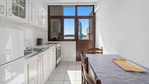 A compact kitchen with white cabinetry, a dining table with a tray, and a view through a large window. - Holiday Apartment GORAN DADIĆ APP 2 (4+0) (Srima)