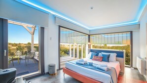Ein modernes Schlafzimmer mit einem großen Bett, Blick ins Freie und einem Balkon mit Gartenmöbeln.