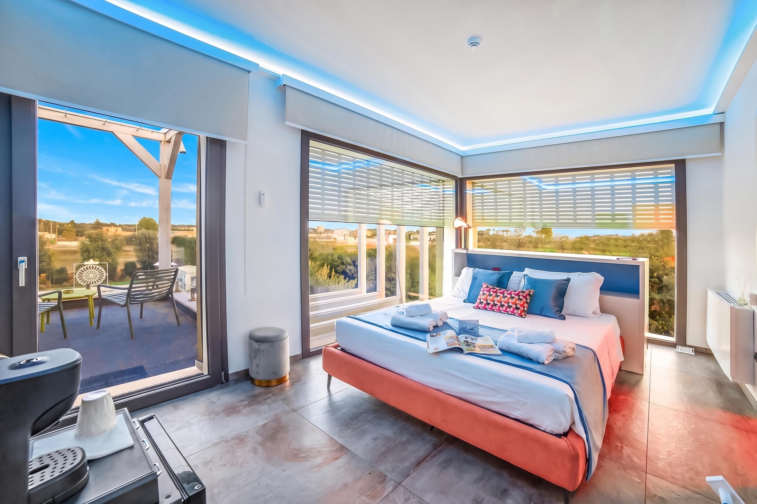 Une chambre moderne dotée d’un grand lit, offrant une vue sur l’extérieur et donnant sur un balcon aménagé avec du mobilier d’extérieur.