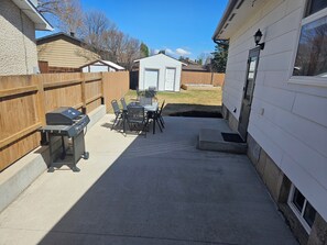 Een achtertuin met een barbecue, tuinmeubilair en een tuinhuis.