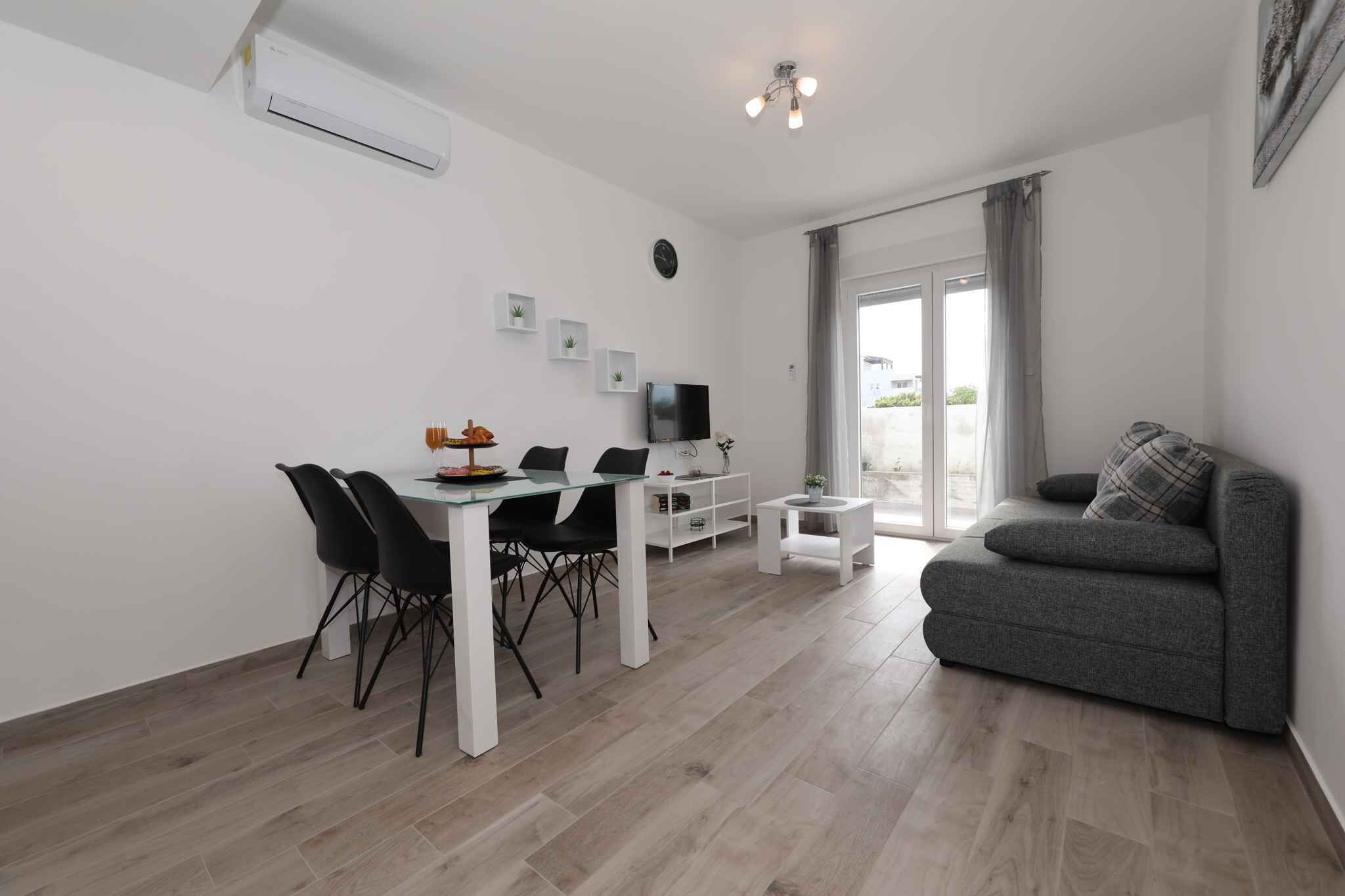 Un salon moderne avec un canapé gris, une table à manger avec des chaises, un téléviseur et une petite table d’appoint blanche.