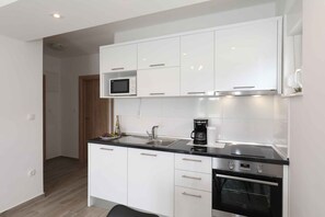 A modern kitchen with white cabinets, a microwave, a coffee maker, and an oven. - Holiday apartment with pool (Seline)