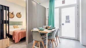 A hotel room with a bed, a dining table set with plates and glasses, a wooden cabinet, and a sliding door with a teal curtain. - GuestReady - New apartment in a quiet area (Valencia)