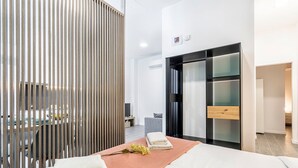 A modern hotel room with a bed, a wooden partition, a TV, and a minibar. - GuestReady - New apartment in a quiet area (Valencia)