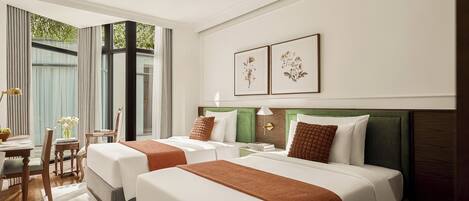 Habitación de hotel con dos camas, una zona de comedor y vistas a zonas verdes.
