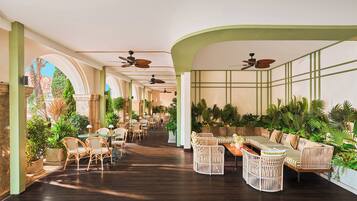 A spacious indoor area with multiple seating arrangements, ceiling fans, and potted plants.