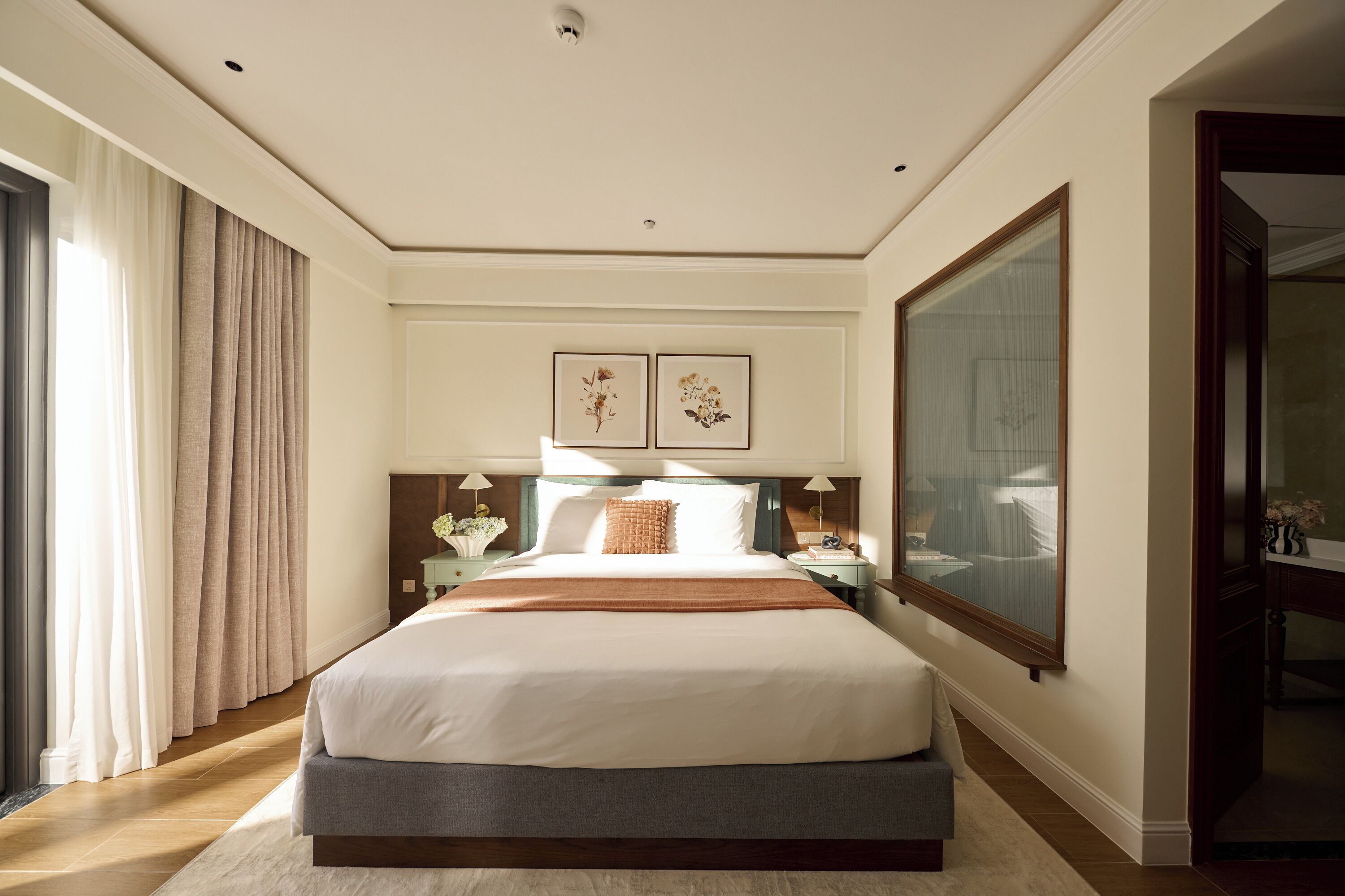 A hotel room with a large bed, a nightstand, a dresser, and a large window.