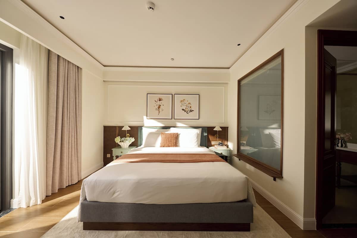 Une chambre d’hôtel avec un grand lit, une table de chevet, une commode et une grande fenêtre.