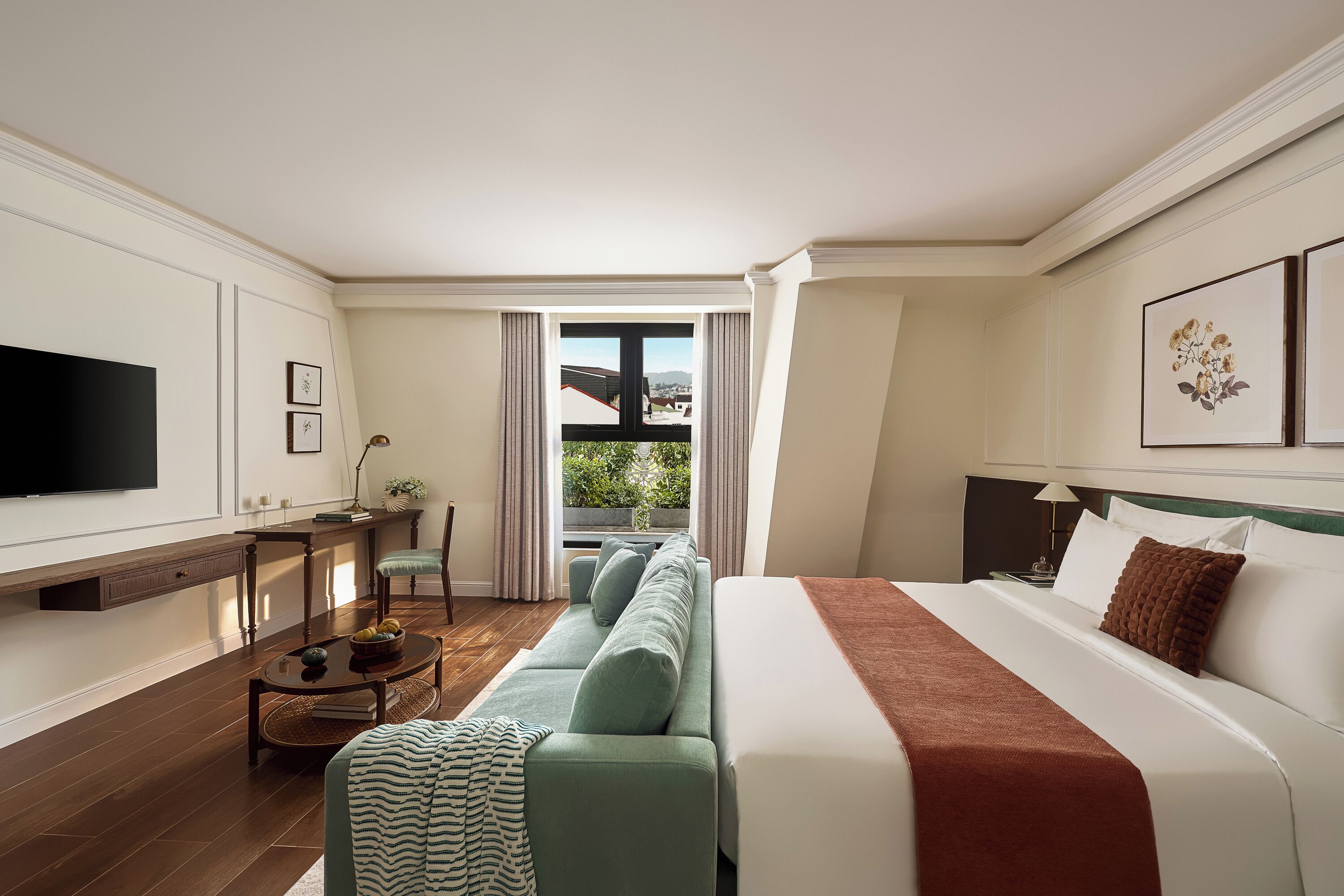 Ein Hotelzimmer mit Bett, einer Couch, einem Fernseher, einem Schreibtisch und Blick ins Freie.