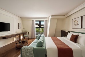A hotel room with a bed, a sofa, a TV, a desk, and a view of the outdoors.