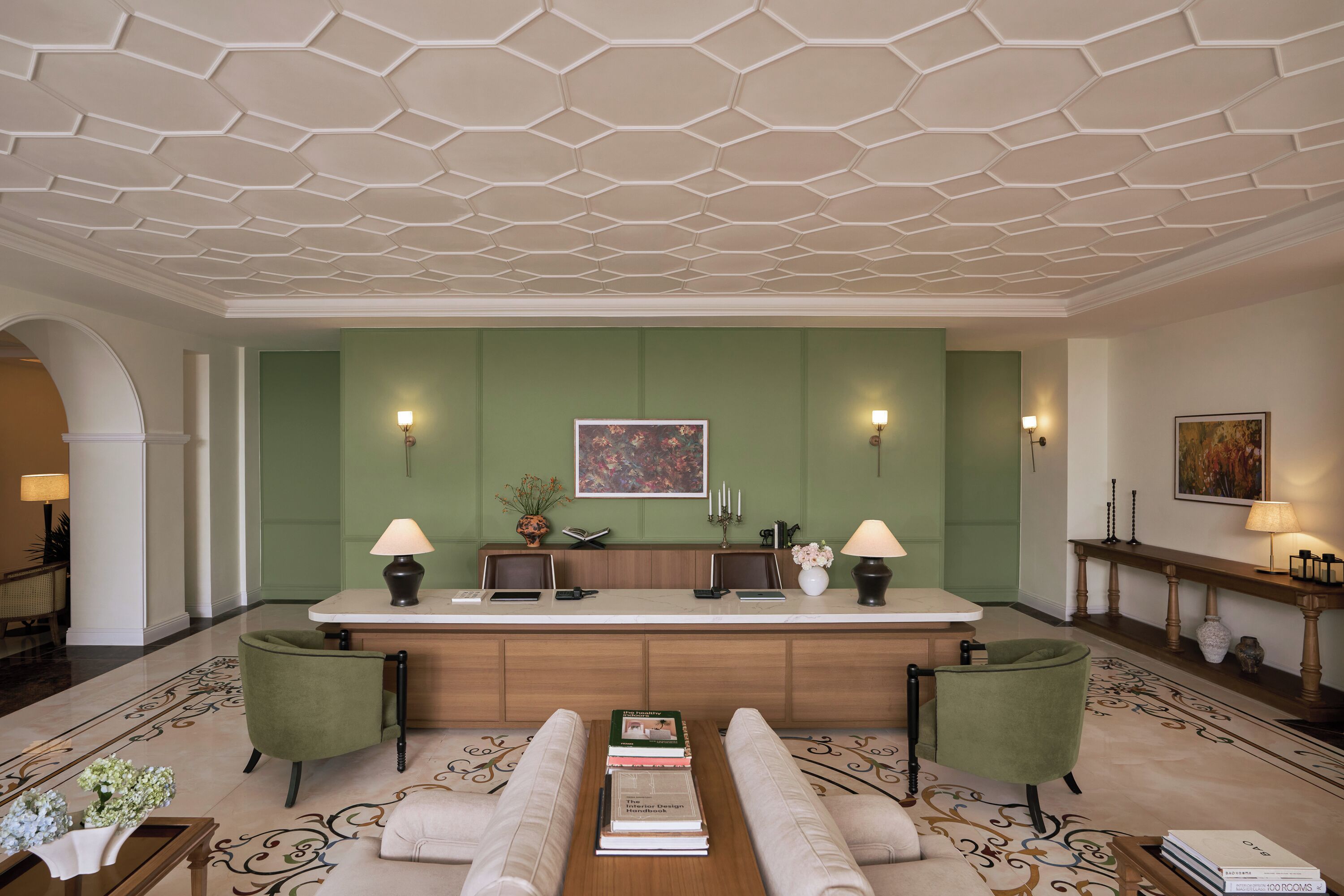 A lobby with a reception desk, green walls, a patterned floor, and a seating area with a sofa and armchairs.