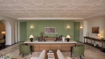 A lobby with a reception desk, green walls, a patterned floor, and a seating area with a sofa and armchairs.