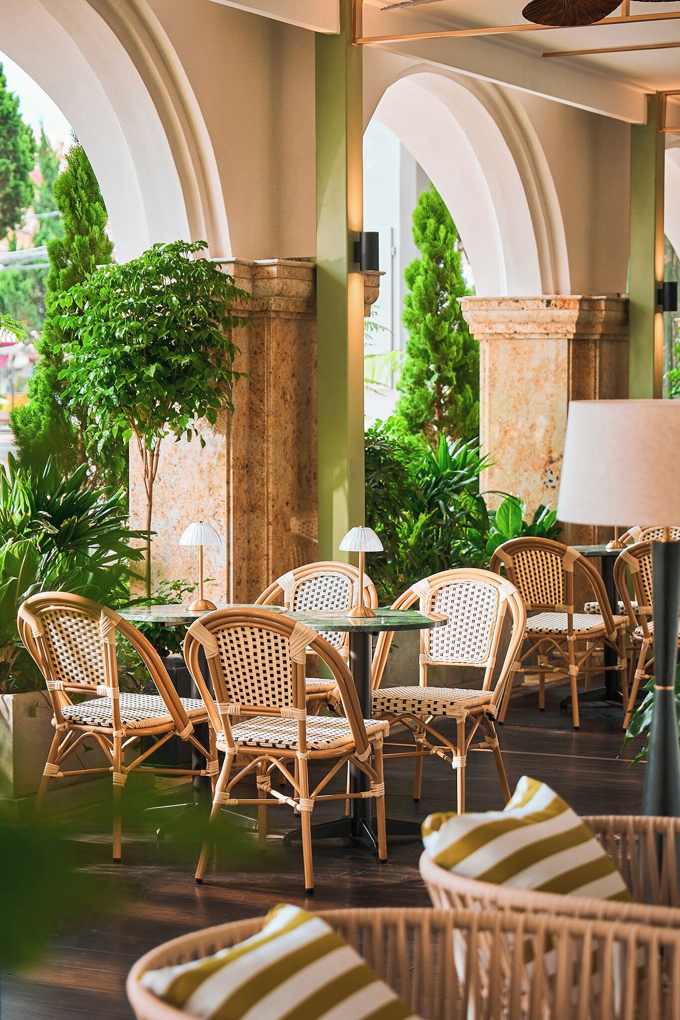 A covered outdoor seating area with wicker chairs, tables, and potted plants.