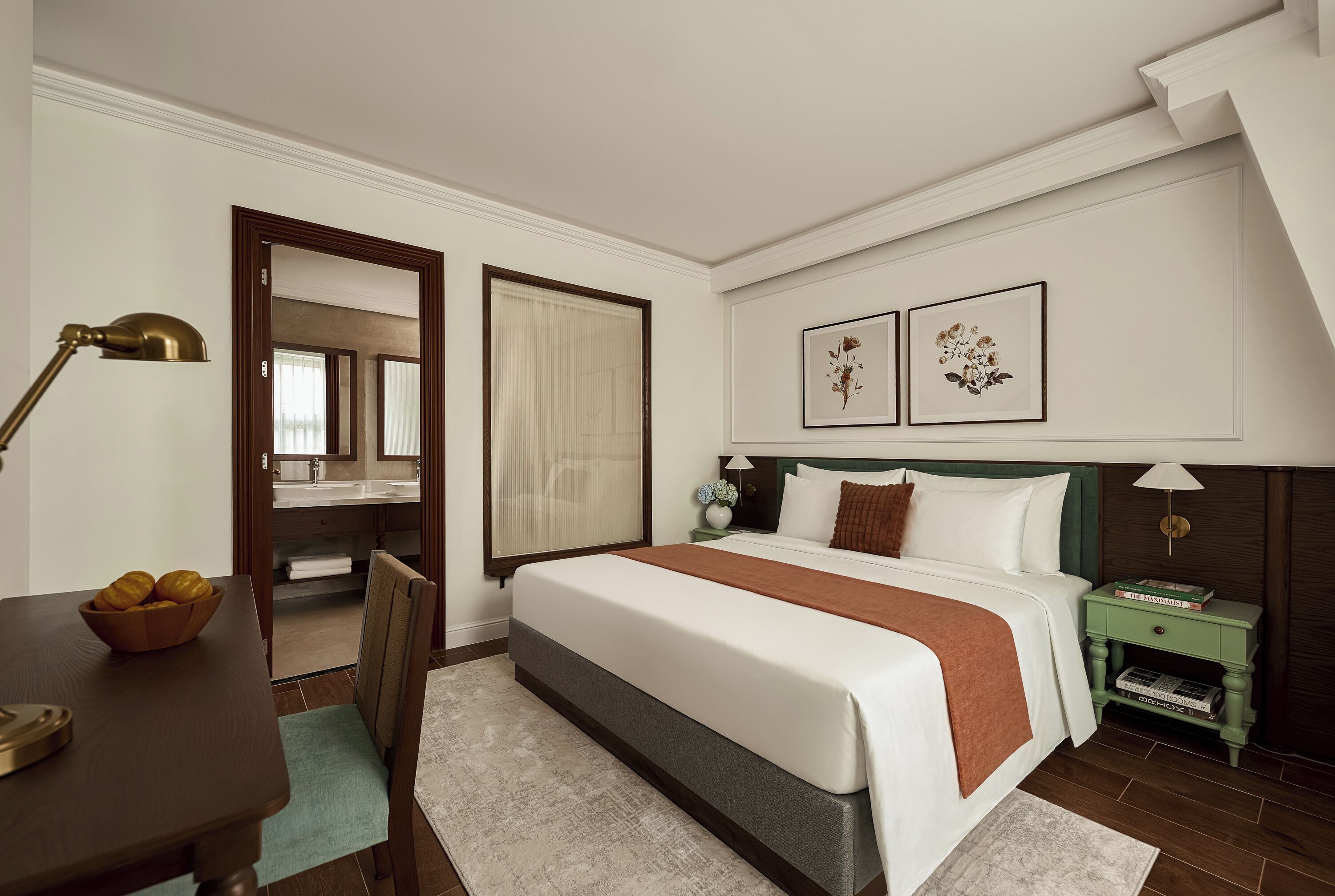 Ein Hotelzimmer mit Bett, Schreibtisch, Stuhl, Nachttisch und Wandlampe.