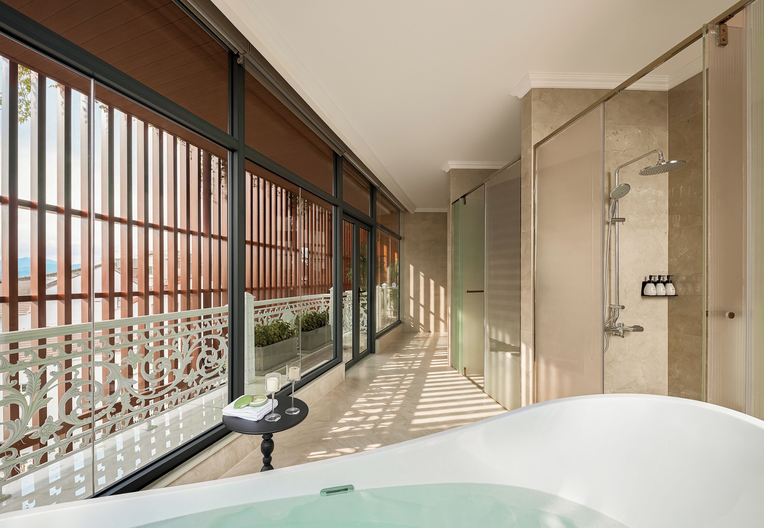 Un baño moderno con bañera, ducha y un balcón de cristal con barandilla decorativa.