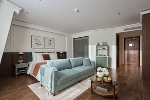 Une chambre à coucher avec un lit, un canapé bleu, une table de chevet, une lampe, une commode et une porte.