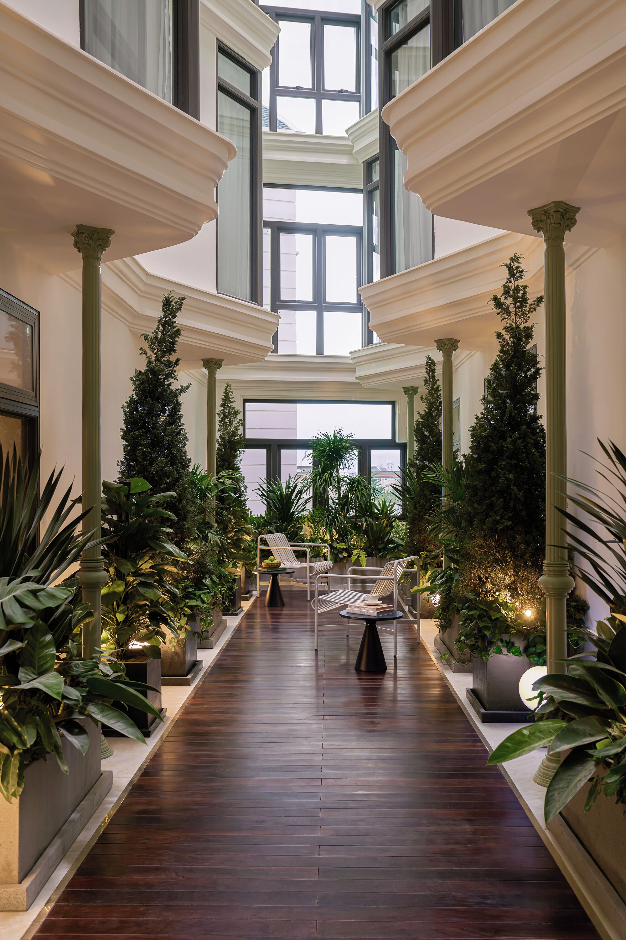 A spacious atrium with a central walkway flanked by columns, surrounded by lush greenery and seating areas.