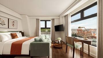 A hotel room with a large bed, a sofa, a desk, and a TV.
