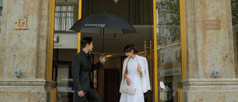 A building entrance with a glass door, a black umbrella, and a car parked in front.