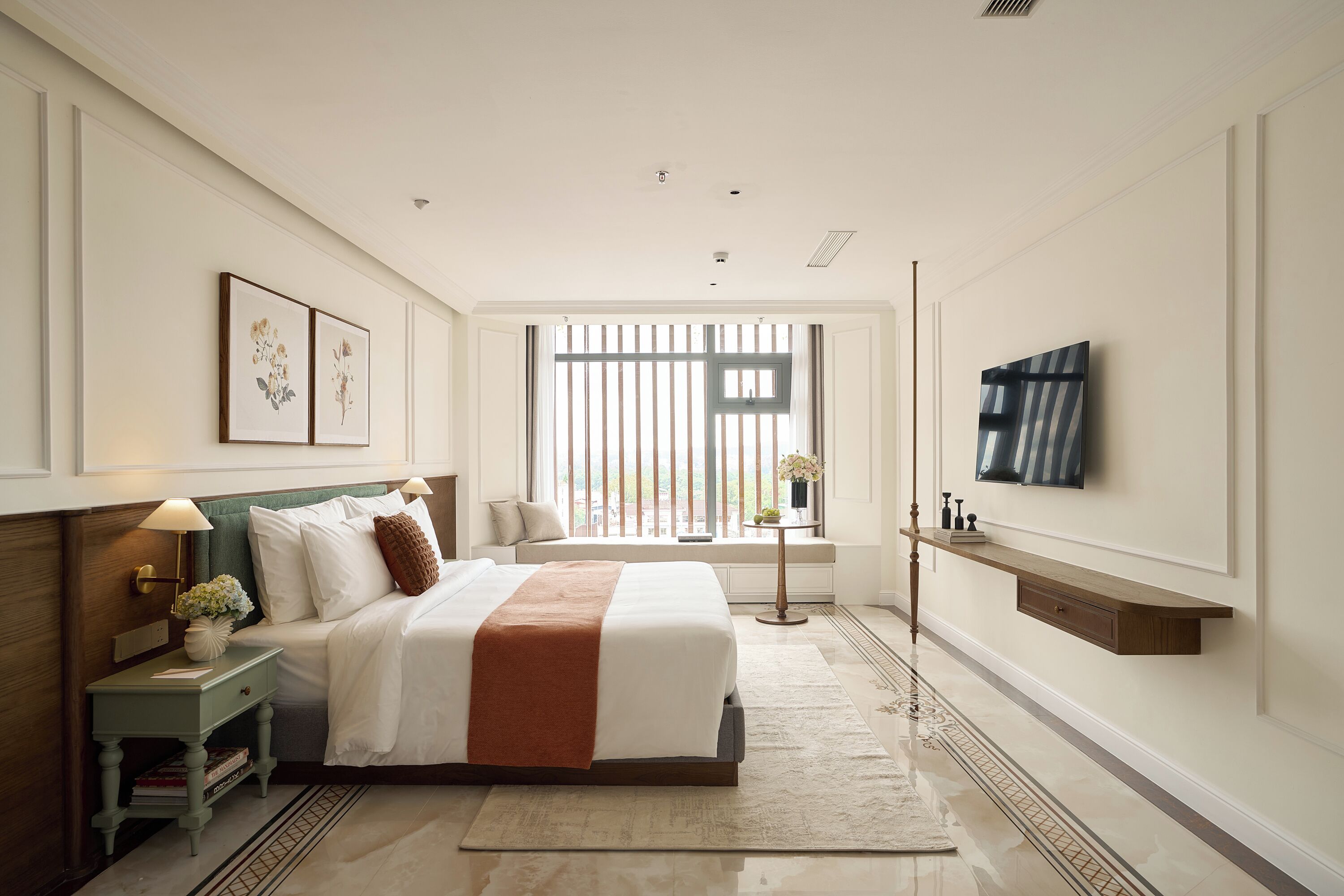 A bedroom with a bed, bedside tables, a TV, and a window with blinds.