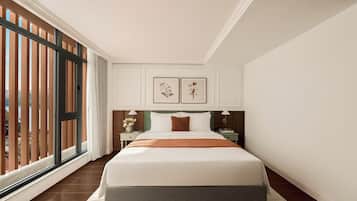A hotel room with a large bed, a nightstand, a lamp, and a view of the outdoors through a sliding door.