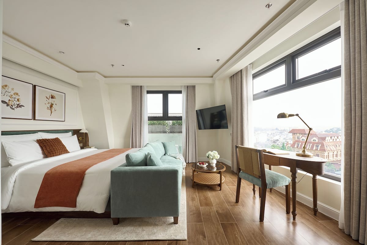 Une chambre à coucher avec un lit, un bureau, une chaise, une télévision et une fenêtre donnant sur la ville.