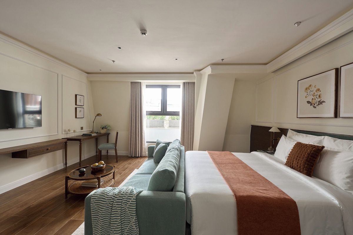 A hotel room with a bed, a TV, a desk, and a window.