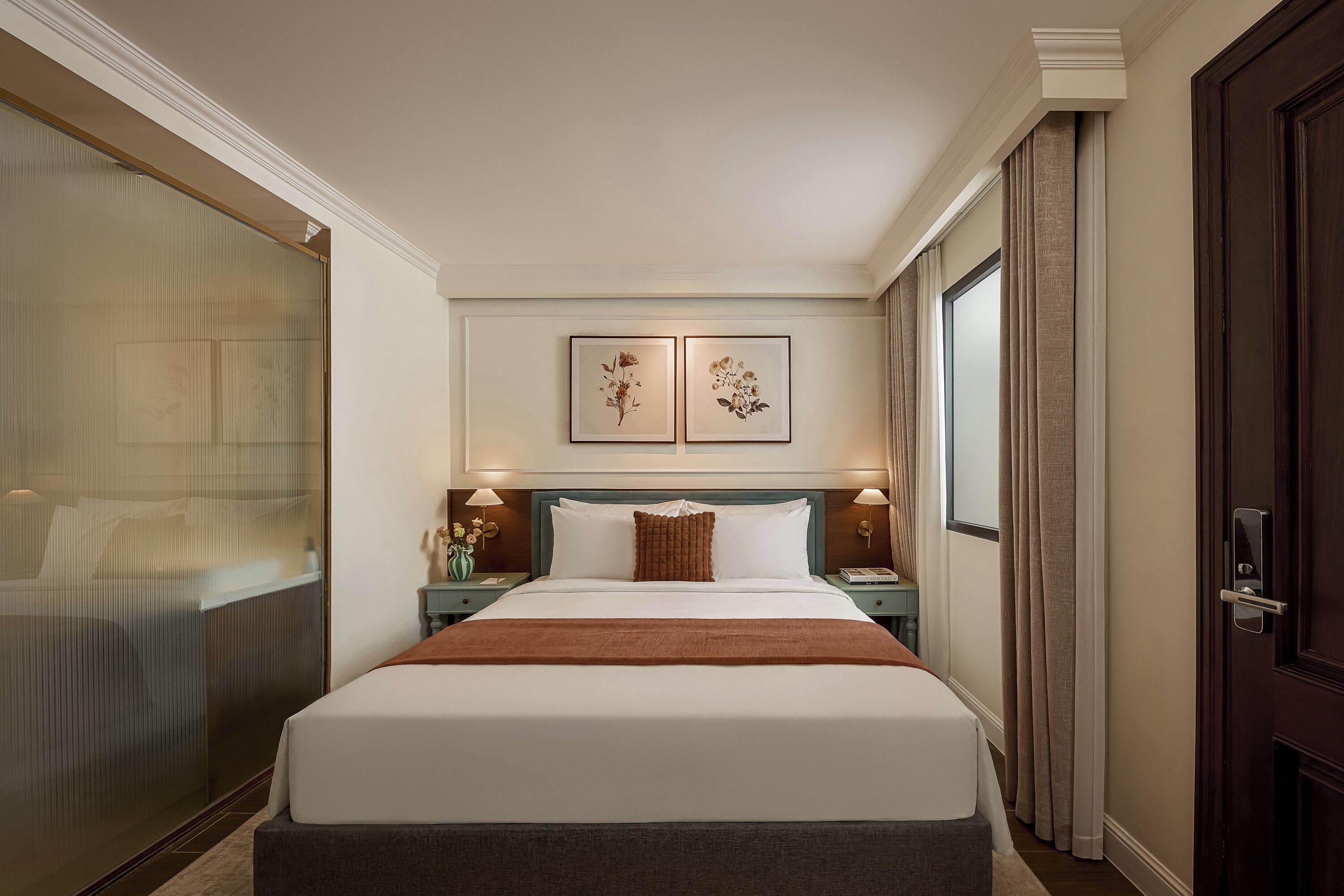 Ein Hotelzimmer mit einem großen Bett, zwei Nachttischen, einem Fenster mit Vorhängen und einer Tür mit Griff.