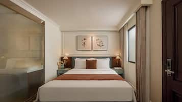 Ein Hotelzimmer mit einem großen Bett, zwei Nachttischen, einem Fenster mit Vorhängen und einer Tür mit Griff.
