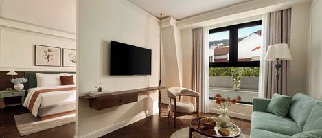 A modern hotel room with a bed, a TV, a sofa, and a view of the city.