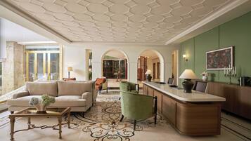 A spacious lobby with a high ceiling, a reception desk, seating area, and a view of the interior through a glass door.