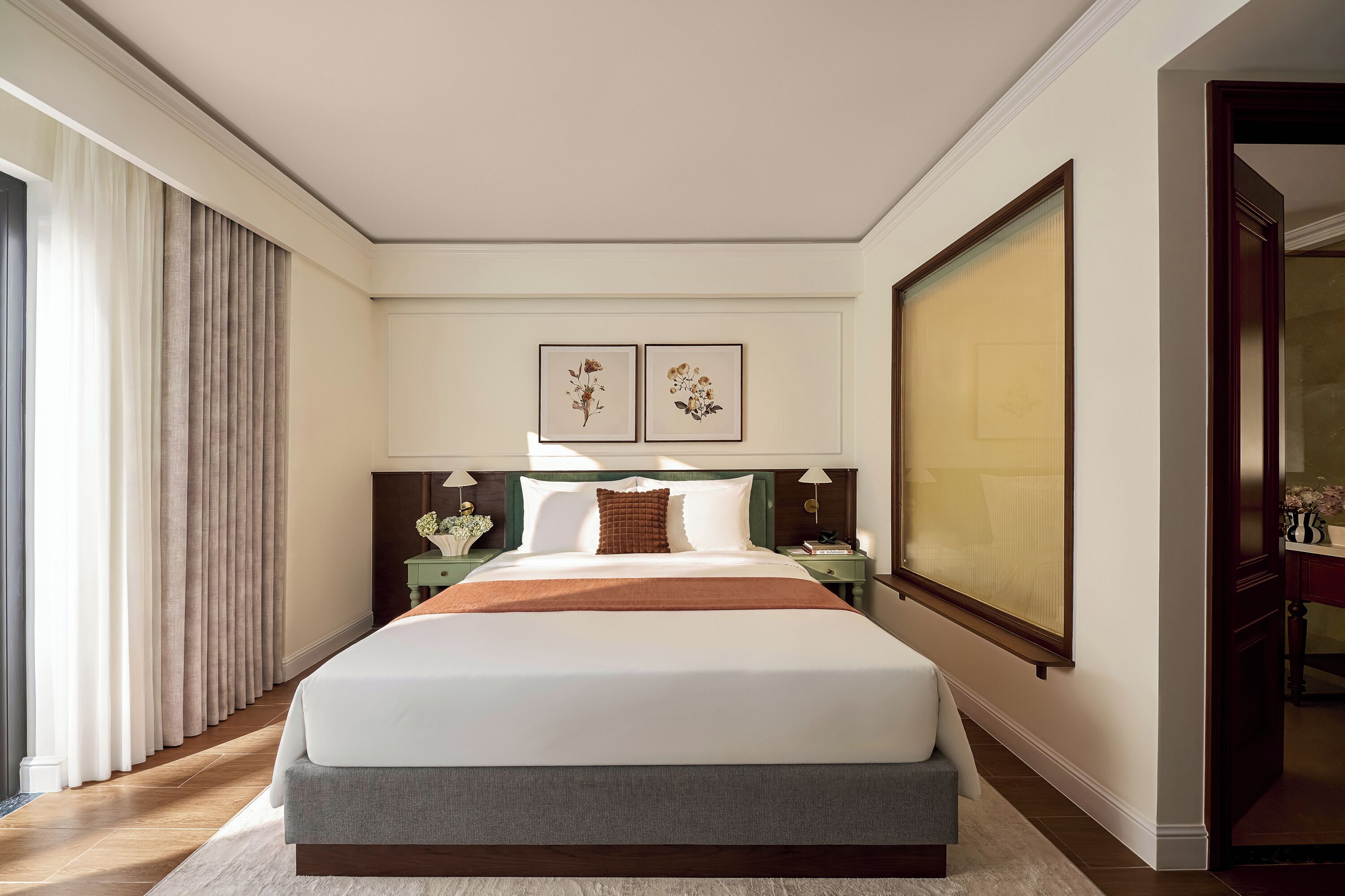 A hotel room with a large bed, a nightstand, a lamp, and two framed floral artworks on the wall.