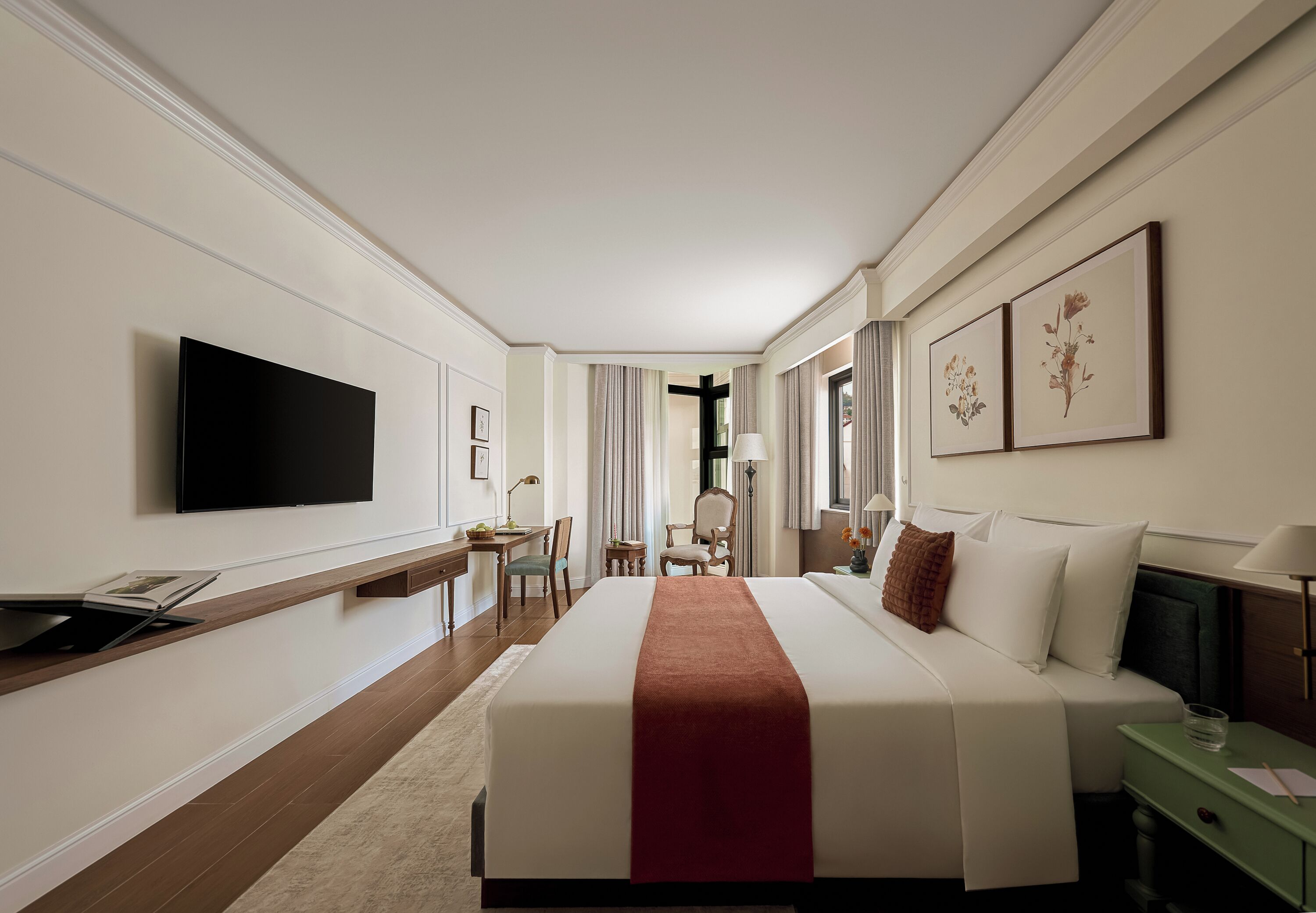 A hotel room with a large bed, a desk with a chair, a television, and artwork on the walls.