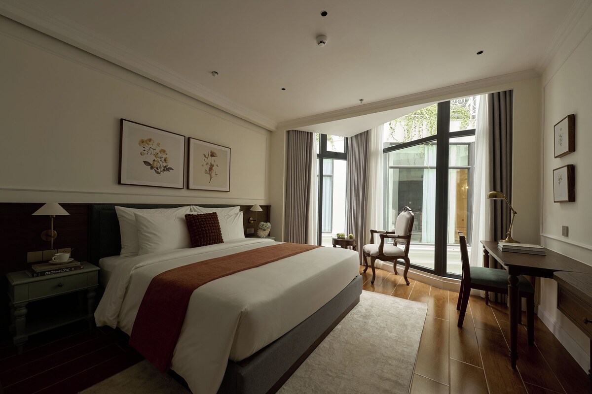 A hotel room with a large bed, a desk, a chair, and a view of the outdoors.