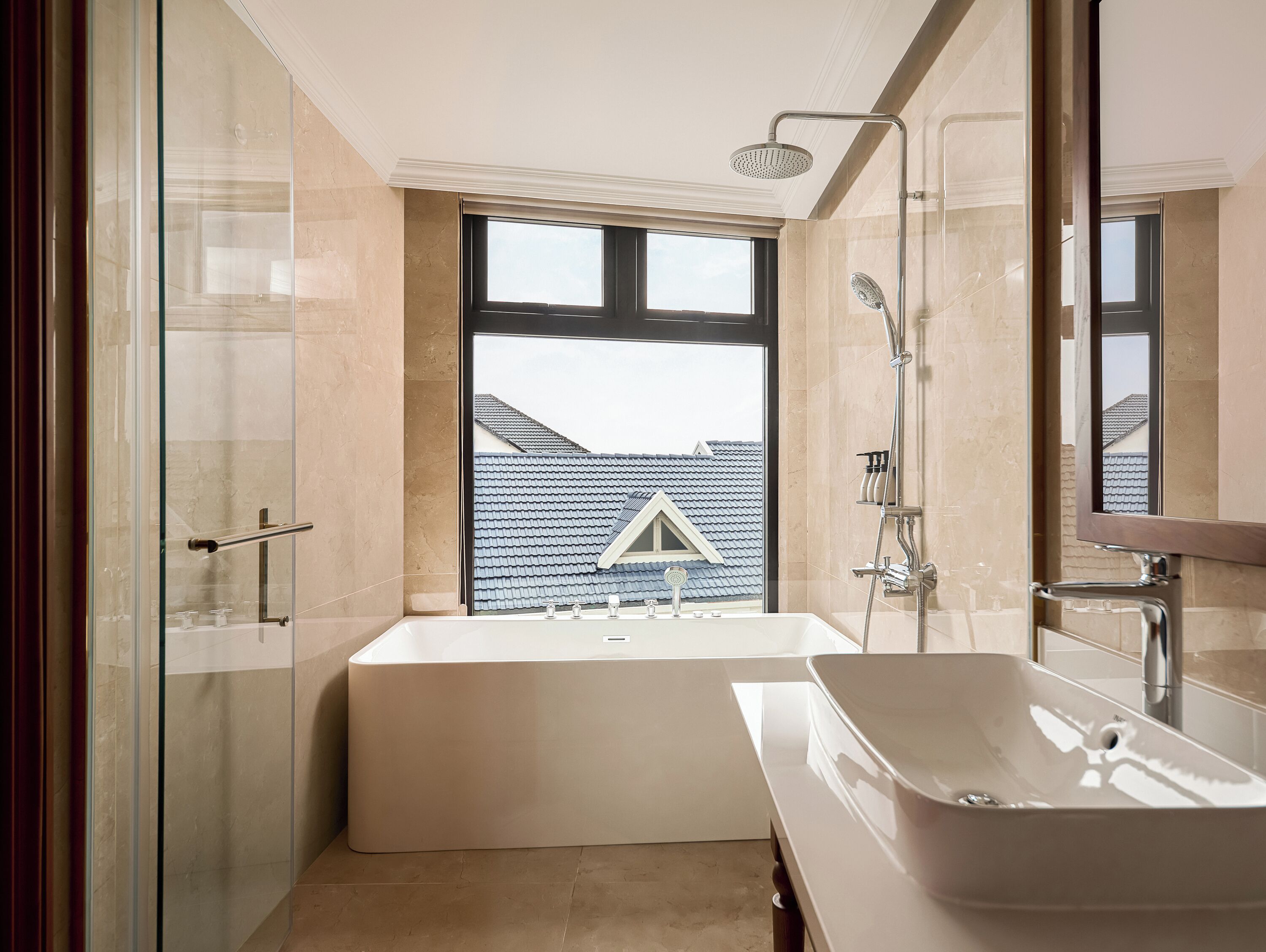 A modern bathroom with a bathtub, a shower, and a large window offering a view of a house.