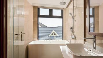 A modern bathroom with a bathtub, a shower, and a large window offering a view of a house.