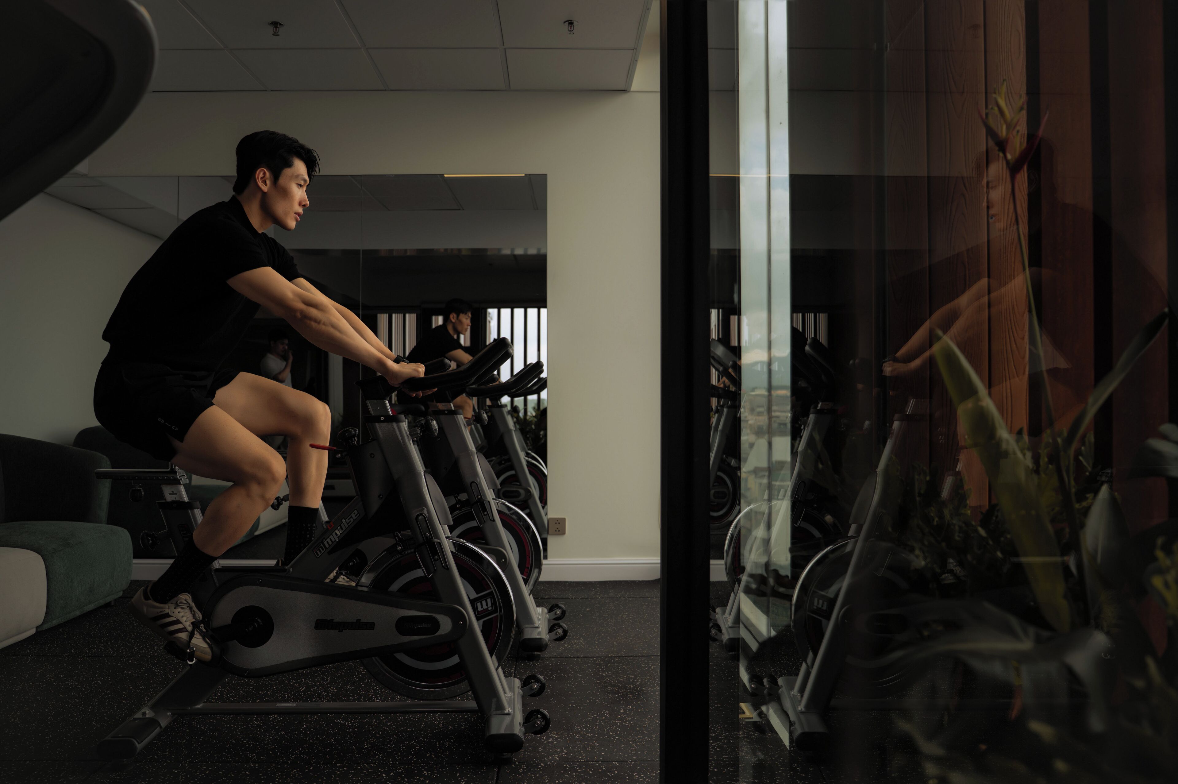 A person using an exercise bike in a gym with multiple bikes and a mirrored wall.