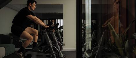 A person using an exercise bike in a gym with multiple bikes and a mirrored wall.