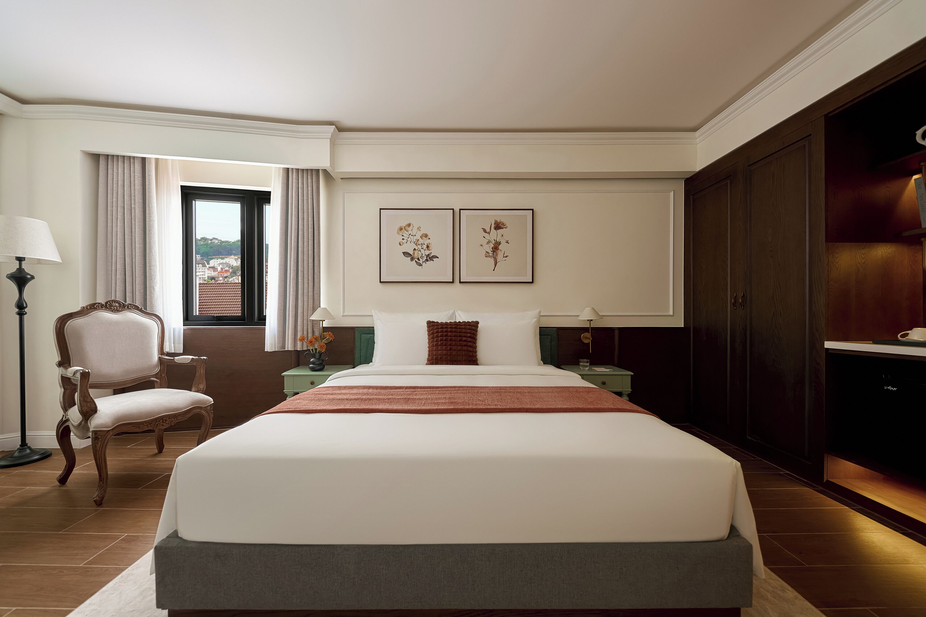 A hotel room with a large bed, a chair, a desk, a lamp, and a view of the outside.
