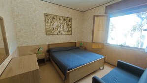 A bedroom with a bed, a desk, a chair, a window, and a wall-mounted artwork. - Conca Verde - Lignano (Lignano Sabbiadoro)