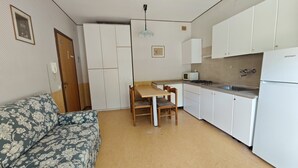 A compact kitchen with a dining table, chairs, a microwave, a stove, and a refrigerator. - Conca Verde - Lignano (Lignano Sabbiadoro)