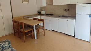 A compact kitchen with a dining table, chairs, a microwave, a stove, and a refrigerator. - Conca Verde - Lignano (Lignano Sabbiadoro)