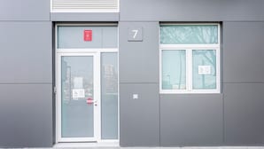 Entrada de un edificio con puerta de cristal, un cartel con el número 7 y una ventana que da a vistas de árboles.